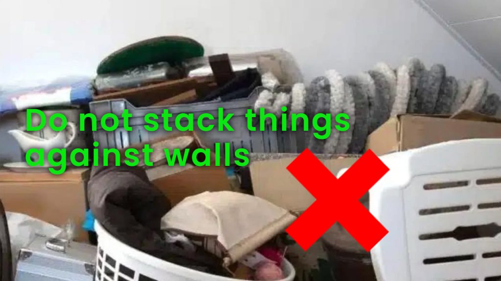 A pile of things against a wall with an x through it. Do not leave things against walls.